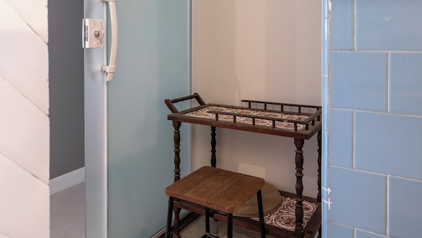 Een hoekzaak met een schuifdeur, een houten bankje en een betegelde muur.