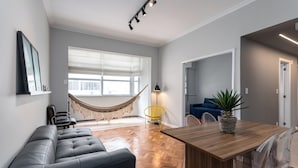 Een moderne woonkamer met een houten eettafel, een zwarte leren bank, een hangmat en een gele stoel.