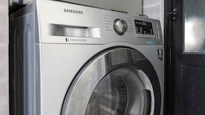 Een Samsung digitale inverter wasmachine in een compacte, praktische ruimte met een betegelde muur en een deur aan de rechterkant.