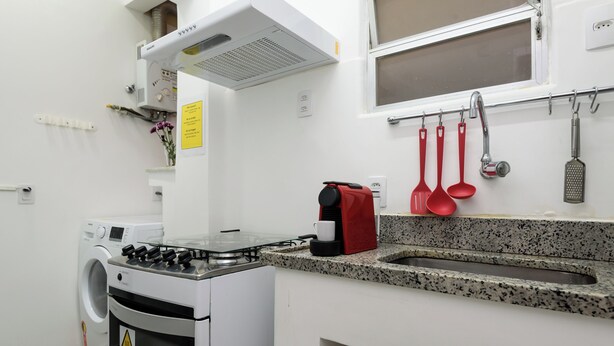 A kitchen with a gas stove, a washing machine, a sink, and various utensils hanging on the wall. - 6 Minutos Da Praia De Ipanema | Gc707 (Rio de Janeiro)