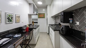 Una cucina moderna con mobili bianchi, piano di lavoro nero e macchina da caffè. Si notano quadri appesi al muro e uno schienale piastrellato.