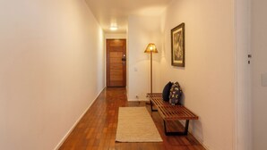 A hallway with wooden flooring, a bench, a lamp, and a door at the end. - 5 Minutos Da Praia Do Leme | Gs1102 (Rio de Janeiro)