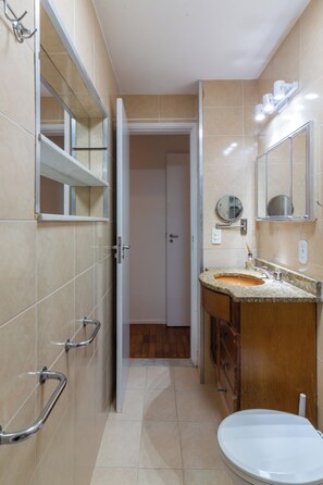 A bathroom with a sink, mirror, and toilet. There are grab bars on the wall and a door leading to another room. - 5 Minutos Da Praia Do Leme | Gs1102 (Rio de Janeiro)