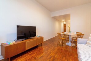 En moderne stue med et fladskærms-tv på et træpanel, et spisebord med stole og en sofa.