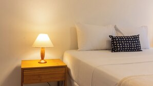 A neatly made bed with white bedding, a small wooden nightstand with a lamp, and a striped rug on the floor. - 5 Minutos Da Praia Do Leme | Gs1102 (Rio de Janeiro)