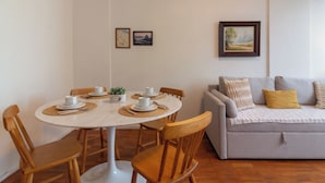 A dining area with a round table, wooden chairs, and a grey sofa with a yellow pillow. There are two framed pictures on the wall. - 5 Minutos Da Praia Do Leme | Gs1102 (Rio de Janeiro)