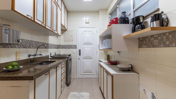 A kitchen with a sink, stove, and microwave. There is a white door in the center. - 3 Minutos Da Praia Do Leme | Gs501 (Rio de Janeiro)