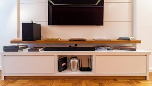 A modern living room with a mounted TV, a white entertainment unit with books and electronic devices, and a wooden floor. - 3 Minutos Da Praia Do Leme | Gs501 (Rio de Janeiro)