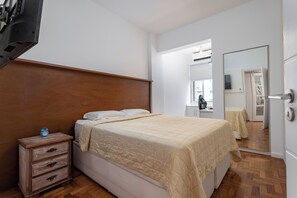 A bedroom with a wooden headboard, a bed with a beige quilt, a nightstand with drawers, and a mirror on the wall. - 3 Minutos Da Praia Do Leme | Gs501 (Rio de Janeiro)