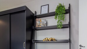 Ein Zimmer mit einem schwarzen Kleiderschrank, einem blauen Sessel, einem Metallregal mit einer Pflanze und einem gerahmten Zertifikat an der Wand.
