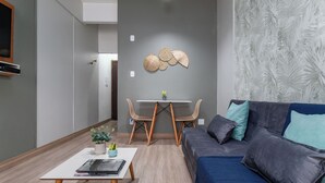 Un soggiorno moderno con un divano blu, un tavolino da caffè con libri e una pianta, una zona pranzo con un tavolo bianco e sedie in legno, e una parete con un motivo a foglia.