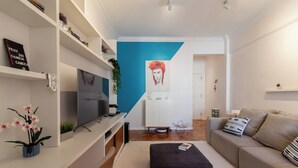 A modern living room with a flat-screen TV, a black ottoman, a beige sofa, and a blue accent wall. - Refúgio Em Copacabana Perto Da Praia | I801 (Rio de Janeiro)