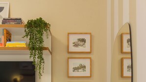 A room with a bed, a TV, a shelf with books and a plant, framed pictures on the wall, and a mirror. - Refúgio Em Copacabana Perto Da Praia | I801 (Rio de Janeiro)