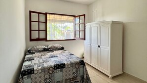 A bedroom with a bed, a wardrobe, a ceiling fan, and a window with a view of greenery. - Refugio Brisa Do Campo | Ig - Solar Do Campo (Iguaba Grande)
