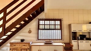 A kitchen with a wooden staircase, a window with bars, and a tiled floor. - Refugio Brisa Do Campo | Ig - Solar Do Campo (Iguaba Grande)