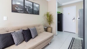 A modern living room with a beige sofa, three framed pictures, a potted plant, and a refrigerator. - Conforto Em Ipanema A 6Min Da Praia | J302 (Rio de Janeiro)