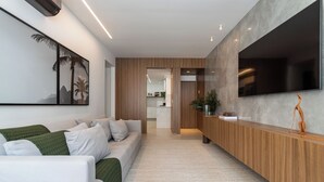 A modern living room with a sofa, a wooden reception desk, and a flat-screen TV mounted on the wall. - 5 Minutos Da Praia De Ipanema | J303 (Rio de Janeiro)