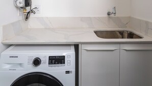 A compact laundry room with a washing machine, a sink, and a water heater. - 5 Minutos Da Praia De Ipanema | J303 (Rio de Janeiro)