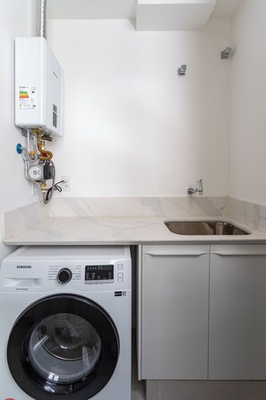 A compact laundry room with a washing machine, a sink, and a water heater.