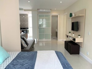 A modern bedroom with a bed, a TV, a sofa, and a sliding door leading to a bathroom. - 6 Minutos Da Praia De Ipanema E Próximo Do Metrô | J801 (Rio de Janeiro)
