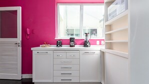 Una cocina con armarios blancos, una pared rosa y una ventana.