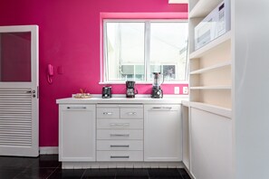 Eine Küche mit weißen Schränken, einer rosa Wand und einem Fenster.