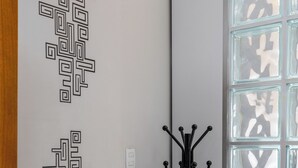 A corner of a room with a coat rack, a patterned wall decoration, and a window with a geometric design. - Estudio Moderno Do Lado De Arpoador | Jc1012 Z2 (Rio de Janeiro)