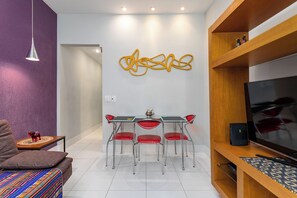 Una sala de estar moderna con una mesa de comedor, sillas rojas, un sofá, un televisor y una obra de arte en la pared.