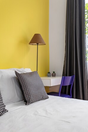 Ein Hotelzimmer mit Bett, Schreibtisch, Lampe, Stuhl und einem Fenster mit Vorhängen.