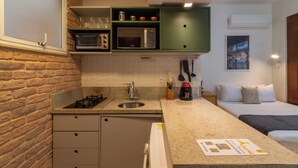A compact kitchen with a microwave, sink, and a small countertop. There is a bed with a pillow and a nightstand with a coffee maker. - 3 Minutos Da Praia Do Arpoador | Jn202 (Rio de Janeiro)