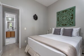 A bedroom with a bed, a large decorative wall piece, and a view into the bathroom. - Encantador Na Barra A 1Min Da Praia | Lc201B (Rio de Janeiro)