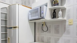 A compact kitchen with a white refrigerator, a microwave, a small shelf with a container, and a chair with a patterned seat. - 3 Minutos Da Praia De Ipanema | Pm203 (Rio de Janeiro)