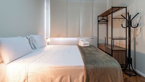 A neatly made bed with white linens, a wooden bedside table, and a wall-mounted coat rack with hangers. - 3 Minutos Da Praia De Ipanema | Pm203 (Rio de Janeiro)