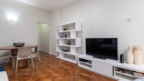 A modern living room with a wooden herringbone floor, a white entertainment unit with a flat-screen TV, and a dining area with a wooden table and chairs. - 3 Minutos Da Praia De Ipanema | Pm203 (Rio de Janeiro)