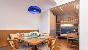 Un coin repas avec une table en bois dressée pour quatre personnes, entourée de chaises en bois. Une suspension bleue est suspendue au-dessus de la table.
