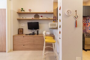 Un espace de vie compact comprenant une télévision, un four à micro-ondes et des étagères en bois.
