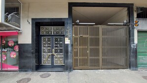 Una entrada de edificio con una reja metálica, una tienda con toldo rojo y un letrero con un número de teléfono.