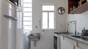 Una cocina compacta con horno integrado, pileta de acero inoxidable y ventana sobre la pileta.