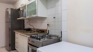 A compact kitchen with white cabinets, a stainless steel refrigerator, a microwave, a gas stove, and a front-loading washing machine. - Beleza No Recreio | Para 5 Pessoas | Sa201 (Rio de Janeiro)