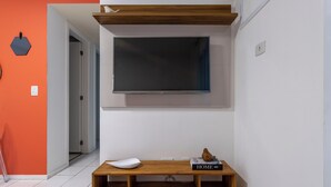 A modern living room with a mounted TV, a wooden bench with a book titled "HOME," and a white chair. - Beleza No Recreio | Para 5 Pessoas | Sa201 (Rio de Janeiro)