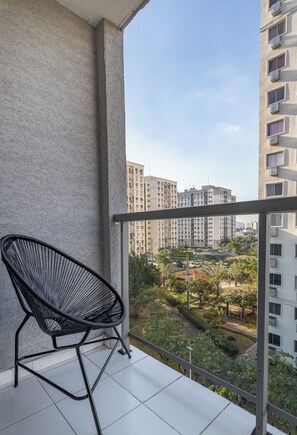 Ein Balkon mit einem schwarzen Stuhl, Blick auf hohe Gebäude und ein grünes Parkgebiet.
