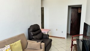 A living room with a brown sofa, a black leather chair, a small table with a red tablecloth, a TV, and a wooden door. - Refúgio Em Salvador Com Vista Para O Mar (Salvador)