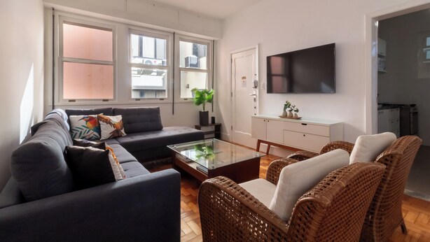 A modern living room with a sofa, wicker chairs, a glass coffee table, and a flat-screen TV mounted on the wall. - Sofisticado A Poucos Passos Da Lagoa | Sb301 (Rio de Janeiro)