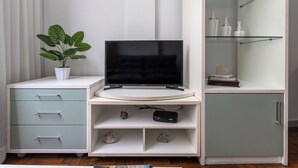 A modern living room with a flat-screen TV, a potted plant, a glass display cabinet, and a cabinet with drawers. - Agradável Em Copa | Ideal Para Amigos | Sc602 (Rio de Janeiro)