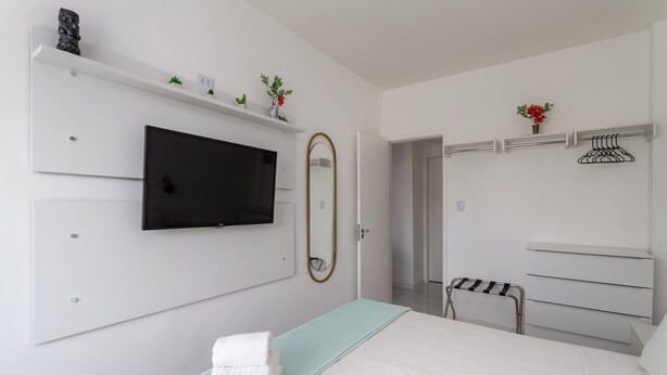 Una camera d'albergo moderna con un letto, una TV fissata al muro, uno specchio, un armadio e una mensola con oggetti decorativi.