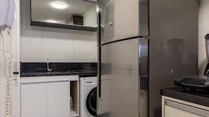 Una cucina compatta con frigorifero in acciaio inossidabile, lavatrice integrata e un piano di lavoro con frullatore.
