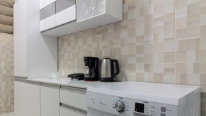 Una cocina compacta con lavadora incorporada, cafetera y salpicadero de azulejos.
