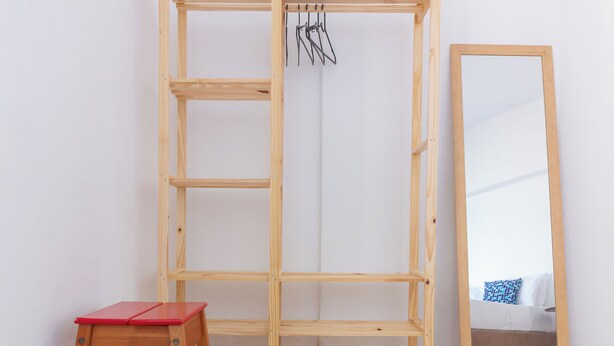 Un armario de madera con estantes, un taburete rojo y un espejo.