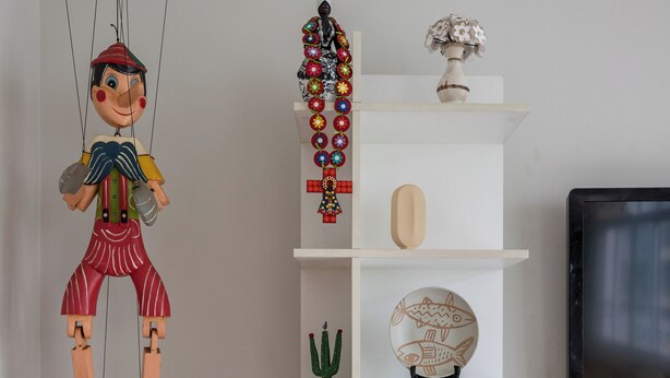 A living room with a white shelving unit displaying various decorative items, a television, and a hanging puppet. - Para Famílias 3Min Da Praia De Copacabana | Sl501 (Rio de Janeiro)