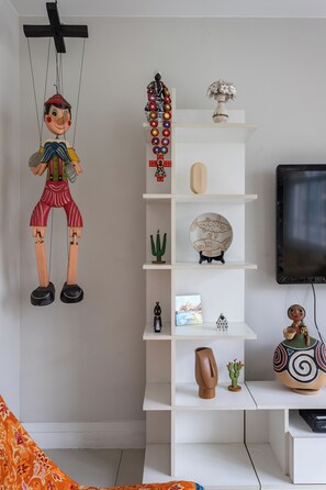 A living room with a white shelving unit displaying various decorative items, a television, and a hanging puppet. - Para Famílias 3Min Da Praia De Copacabana | Sl501 (Rio de Janeiro)
